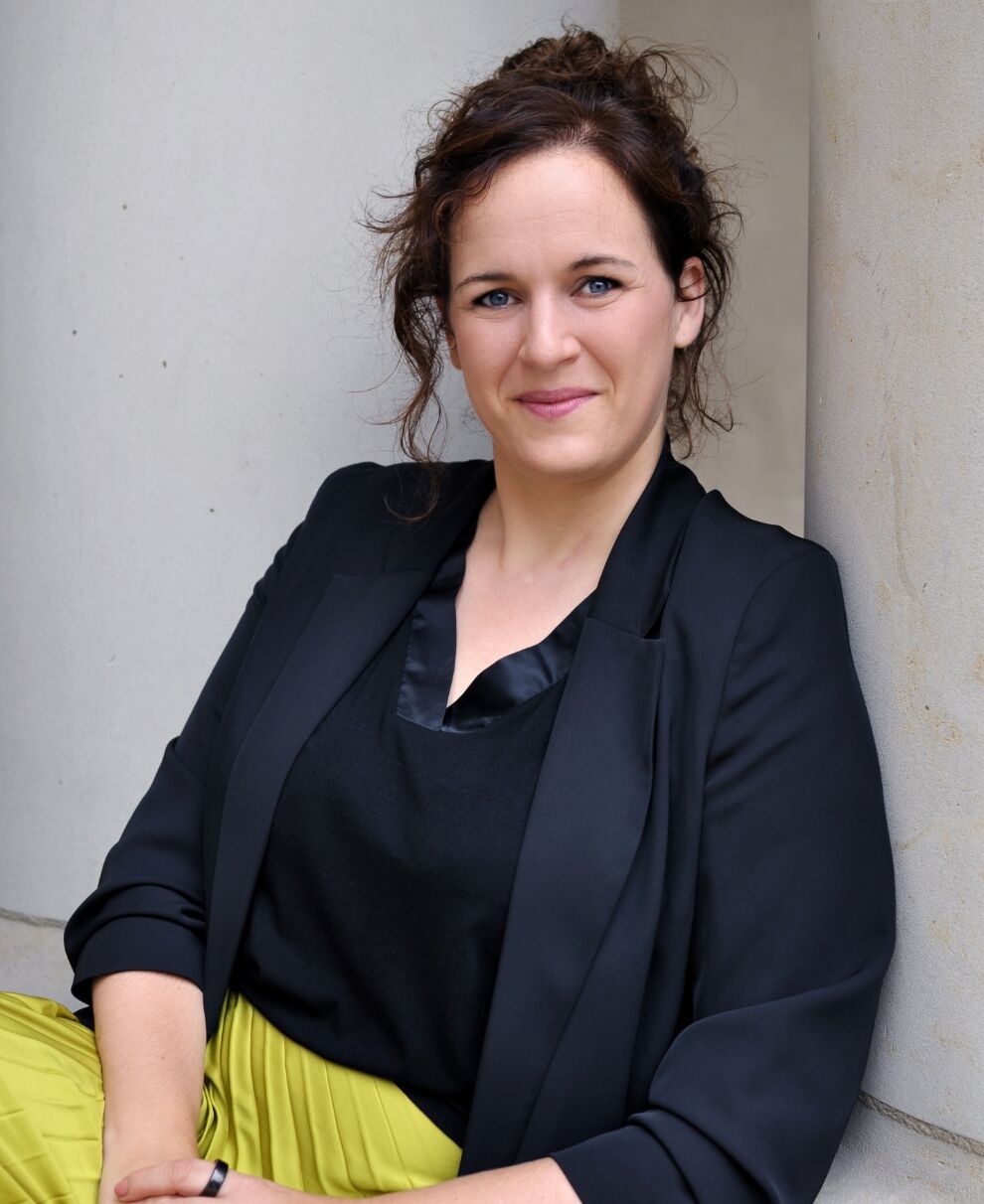 Katrin Terwiel sits leaning against a building and smiles.